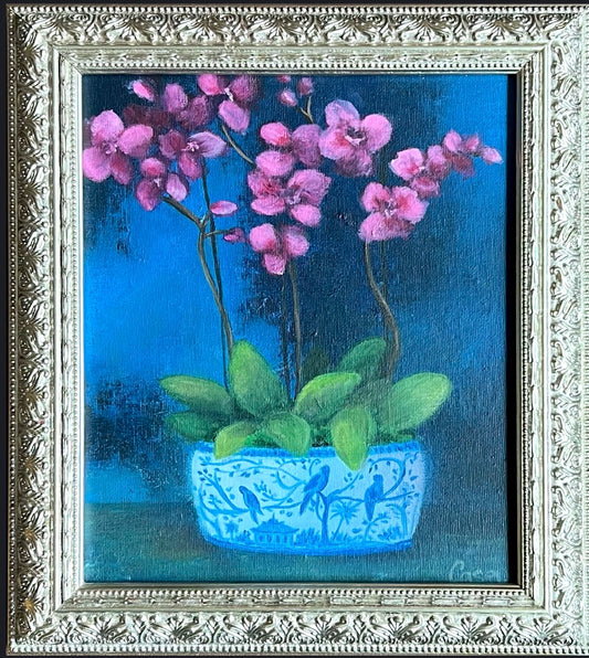 Framed oil painting titled Framed Orchid Elegance, featuring pink orchids in a blue chinoiserie-style planter, set against a deep blue background.