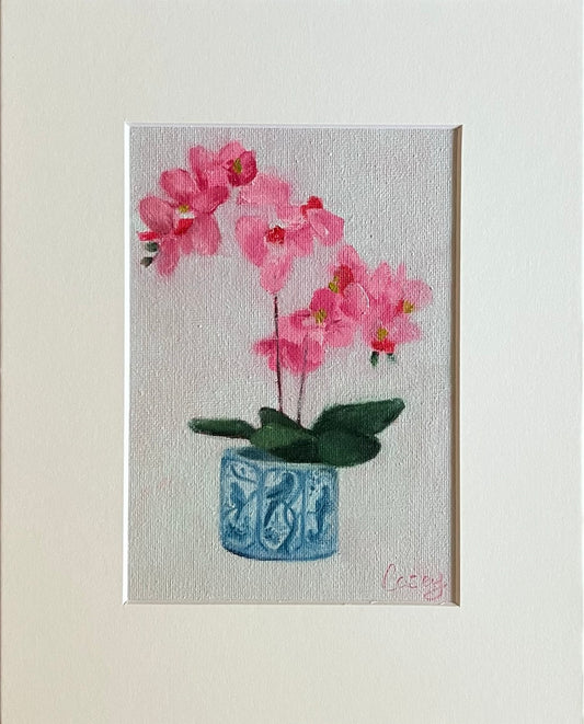 Original oil painting titled Orchid Simplicity, featuring pink orchids in a blue patterned pot on a white background, matted and ready to frame.
